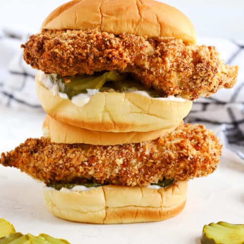 chicken sandwiches with pickles laying around them.